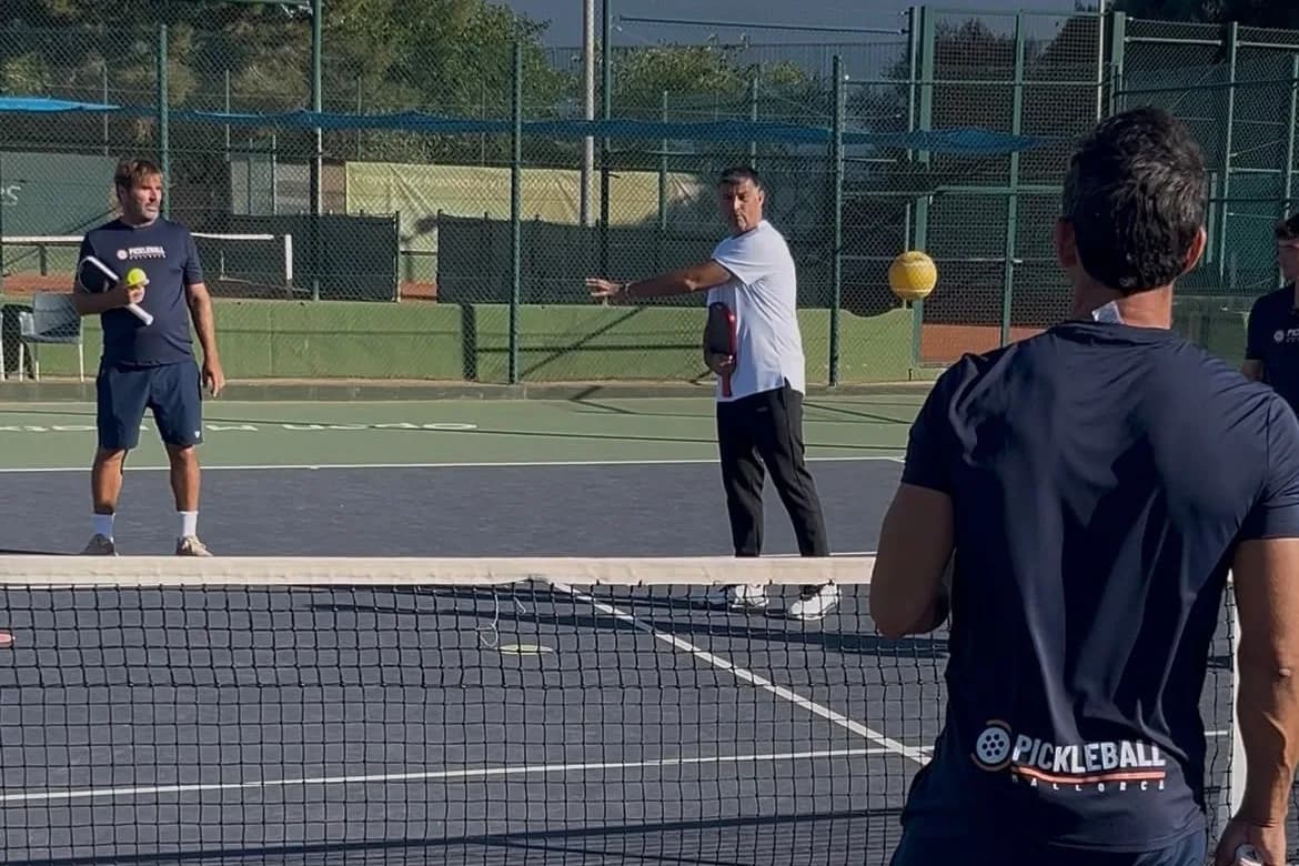 Coach demonstrating a stroke at the net while players look on, on an outdoor pickleball court in Marratxí