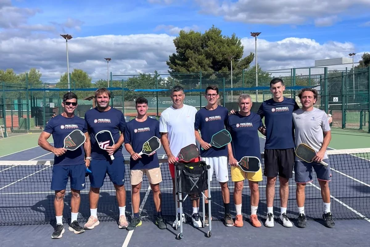 Eight coaches and players standing in a line at the net on an outdoor court, holding paddles