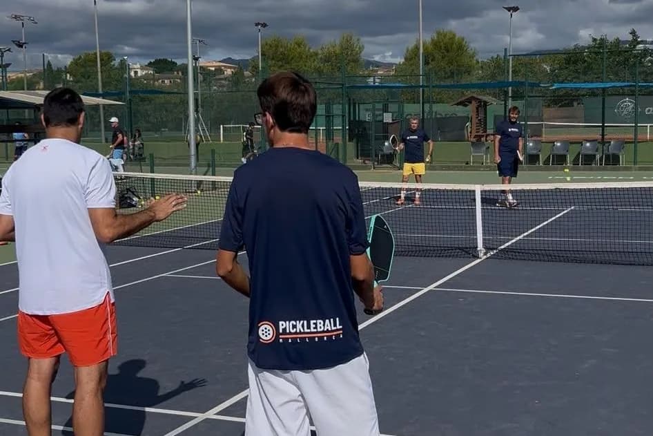 Coach and player at the net watching a rally on an outdoor pickleball court